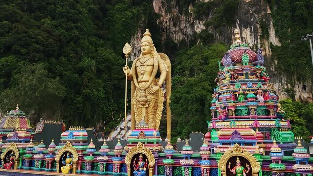 Golden murugan statue overlooking limestone cave temple entrance, landmark hinduist religious site near kuala lumpur, malaysia
