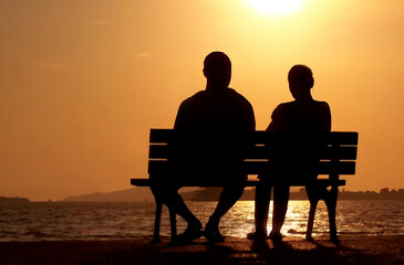 Couple in silhouette seated on a bench in contemplation in front of a lake at sunset. Quiet and peaceful Valentine day moment