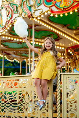 a child in an amusement and amusement park, a happy girl eating cotton candy and enjoying the...