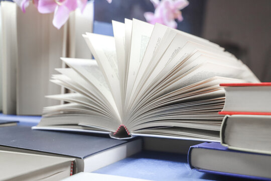 stack of books with orchid, close up. Open book on the table in library. Back to school concept. Open book on table with blur bookshelf background