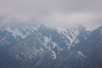Fototapeta premium High mountains under snow. Snow-capped mountain peaks. Epic mountain landscape and dramatic sky. Mountain peaks in winter