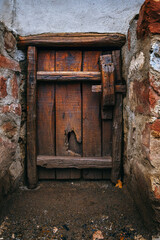 Weathered Rustic Wooden Barn Door in Ancient Stone Wall. Atmospheric Photography of Historical Farm Architecture with Vintage Wooden Animal Entry and Textured Stone Masonry