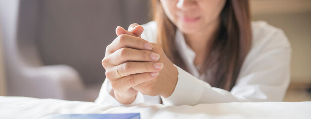 Pray and bible concept. Hand in hand together on bible. Asian woman (worship christian), thinking and closed her eyes. Person front view, female praying, hope for peace-horizontal banner.