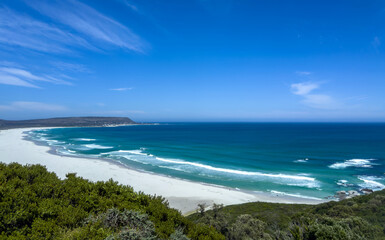 Noordhoek beach near Cape Town, South Africa.  Ocean waves roll in white sand Beach, blue sky