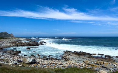 Ocean waves crashing on rocky coast, blue sky with clouds