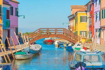 Wooden bridge over Burano’s colorful canal and docked boats