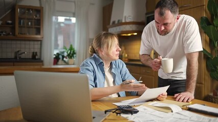A husband and wife are arguing in the kitchen, pointing out errors in documents. The scene captures a tense moment of discussion about bills and financial issues in a household setting. - Powered by Adobe