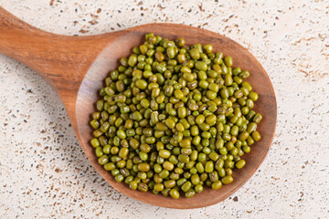 Mung beans in a wooden spoon on beige kitchen table background. Healthy plant-based protein, healthy cooking ingredient for vegan recipes and vegetarian diets, close up