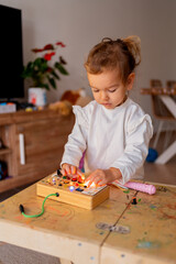Little girl exploring an electronic busy board, developing fine motor skills and problem solving abilities in a playful home environment