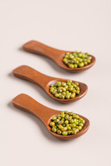 Organic mung beans in a wooden spoons on beige background. Healthy plant-based protein, healthy cooking ingredient for vegan recipes and vegetarian diets