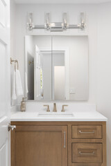 A bathroom detail with an oak cabinet, bronze faucet on a white marble cabinet, and chrome light fixture mounted above the rectangular mirror.