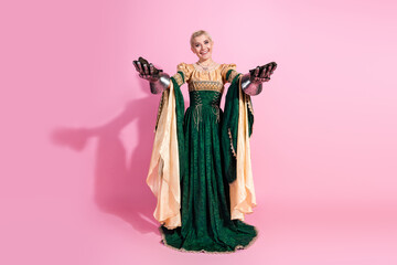 Elegant young woman in medieval attire holding metal gauntlets against a pink background for...