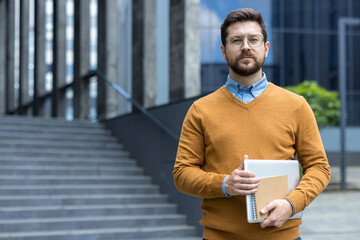 Portrait of a young self-confident businessman and lawyer man standing near the courthouse, holding...