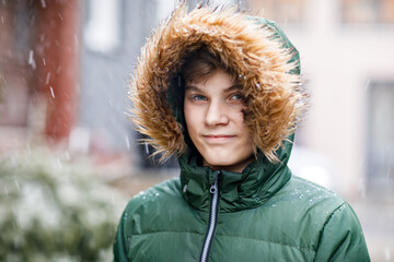 Portrait of teenager school boy outdoors in winter. Beautiful happy child looking at the camera. Schoolboy smiling. Snowing background