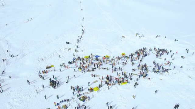 Aerial drone shot of crowd of people in colourful clothes at skiing point near golf course eating, skiing, sledding and walking showing this popular tourist spot in gulmarg kashmir