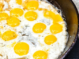Sizzling fried quail eggs in a skillet create a delightful culinary experience at a cozy kitchen setting