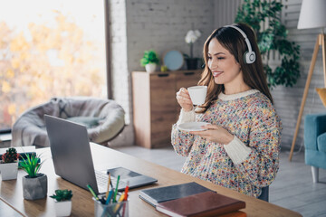 Woman in a cozy home setting enjoying coffee while wearing headphones