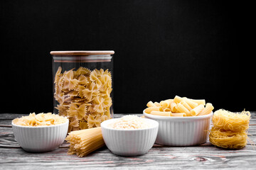 Set of different types of dry pasta on a wooden surface with a black background.