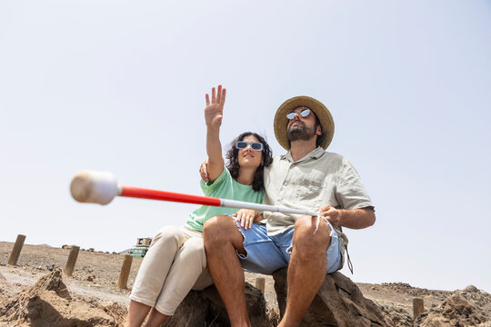 Blind Man and Woman Pointing Ahead While Sitting on Rocks