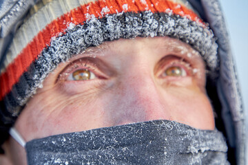Portrait of a mature man in a knitted hat and a mask on his face in close-up in the cold.A man looks away on a very cold and frosty day