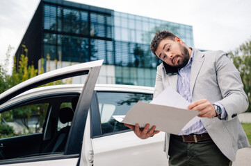 Fototapeta premium Stressed businessman having phone call reading documents next to car
