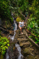 A woman finds peace and relaxation next to a stunningly beautiful waterfall, enveloped by tropical plants, capturing the serene essence of natures tranquility, Tumpak Sewu waterfall, Java, Indonesia