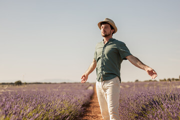 Young attractive man with open arms enjoying the calm and breathing the pure air of nature in the lavender flower field at sunset.