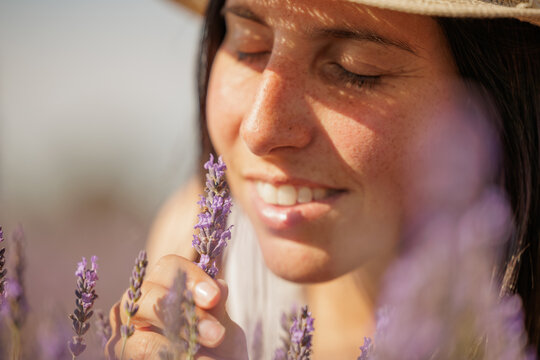 Young woman smiles while enjoying the soft aroma of lavender. The young girl has her eyes closed to smell the fragrance