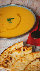 Overhead view of a bowl of soup served with naan bread, styled on a bright wooden table.