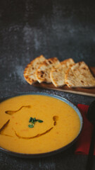 A moody 45-degree shot of a delicious bowl of soup paired with naan bread, styled in a dark and restaurant  like setting.