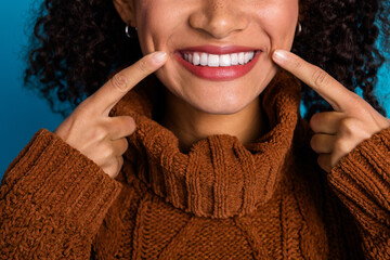 Close-up of a cheerful woman smiling and highlighting her dimpled cheeks, wearing a knitted brown...
