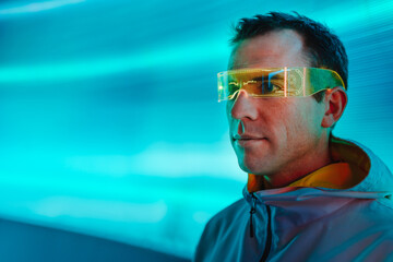 Surreal portrait of man using glowing virtual reality glasses standing in front of neon lights...