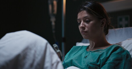 Concentrated female patient in hospital ward looks at window waiting for doctor.