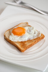 Scrambled eggs on toaster fried bread on quadrangular white textured plate on white table, top view.