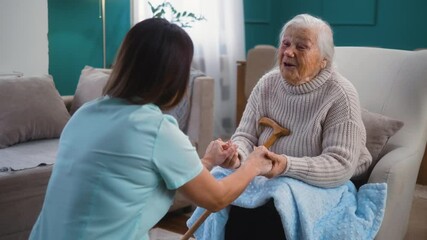 Satisfied 80s senior woman patient holding hands and talking with a female caregiver or nurse at home