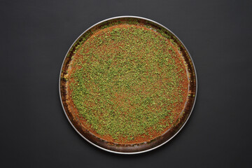 A beautifully prepared tray of traditional Kunafa dessert topped with finely chopped pistachios, showcasing a delicious Middle Eastern delicacy on a dark background for a striking visual presentation.