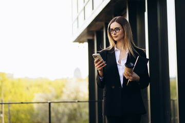 Woman secretary holding laptop and coffee and using mobile phone