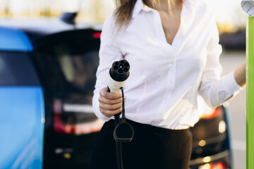 Business woman charging her electric car and holding plug