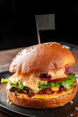 A delicious gourmet burger featuring a juicy patty, fresh lettuce, tomatoes, and red onions, all topped with a creamy sauce, served on a toasted sesame seed bun on a black plate.