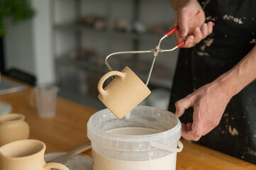 Close-up of a potter's hands glazing a ceramic mug. 