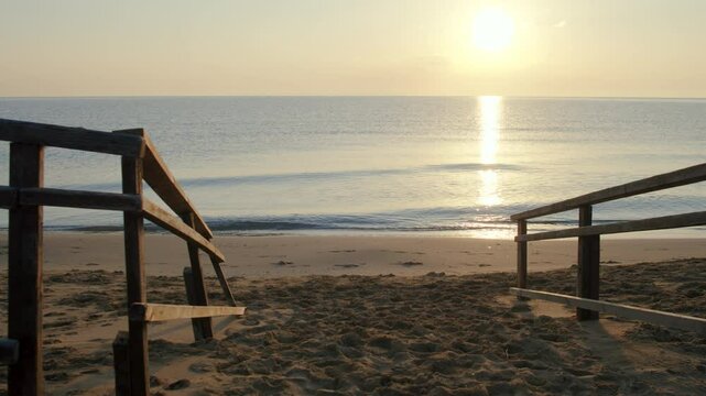 Road to the beach over the wooden old bridge, footprints on the sand, sunset on the sea and the glare of the sun on the water