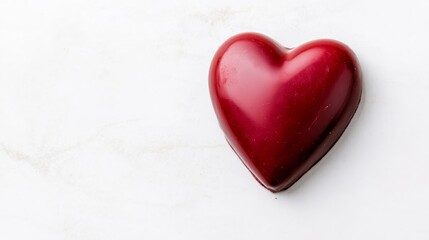 Fototapeta premium Red Heart Shaped Chocolate Candy - Single red heart-shaped chocolate candy on white marble background. Perfect for Valentine's Day or romantic occasions.