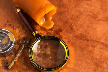 Old compass, key, magnifying glass and candle on brown background.