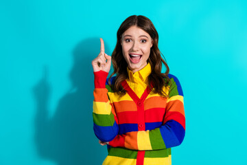 Smiling young woman in rainbow cardigan gestures excitedly on a vibrant teal background