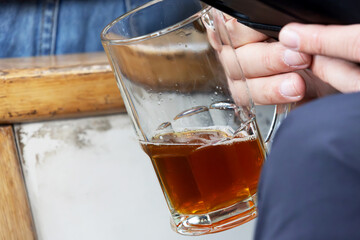 A person holding a mug of beer while using a cell phone that only shows part of it