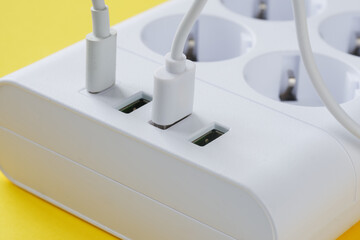 USB ports with plugged-in connectors and electrical outlets on a modern charging station placed on a bright yellow surface. Photo. Selective focus