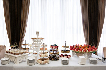 A beautifully arranged dessert table features a variety of sweet treats, including cakes, pastries, macarons, and fresh fruit. The setting is elegant and sophisticated, ideal for a celebration.