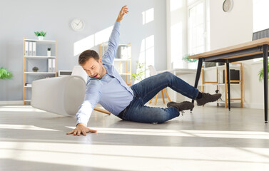 Full body photo of a young clumsy brunette man wearing casual clothes falling down to the floor and...