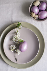 Easter eggs in lilac color on plate with cherry blossom branch. Easter table setting idea