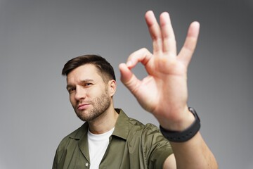 Man making an okay gesture with his hand while posing against a neutral background indoors